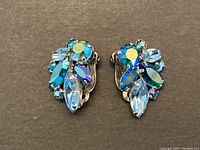 Front view of the pair of vintage Sherman earrings showing blue and iridescent rhinestones in various shapes clustered.