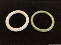 Both jade bangles, one white and one green, placed side by side on a black surface to show color and shape.