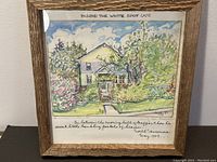 Framed artwork depicting a house with lush garden, captioned 'Behind the White Spot Cafe' with signed text and date 'May 1989.'