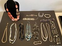 Full overview of vintage costume jewelry lot showing various necklaces, bracelets, and earrings arranged on a black surface.