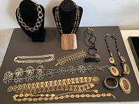 Overview photo of eleven vintage costume jewelry pieces displayed on black surface, including necklaces on stands and various bracelets.