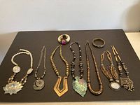 Overview of 8 pieces of costume jewelry displayed on a black surface including necklaces and bracelets, showing varying lengths and pendant styles.