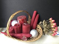 Wicker basket holding multiple red beeswax candles, silver balls, and artificial flowers arranged next to basket