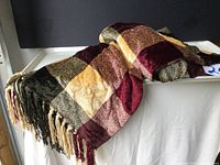 Photo showing a chenille throw blanket folded with visible tassels in beige, burgundy, brown, and black color blocks.