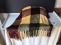 Full view of folded chenille throw showing checkered pattern with burgundy, mustard yellow, cream, and black squares, and multicolored fringe tassels.
