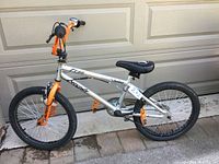 Side view of a children's bike with silver frame and orange accents against a beige garage door.
