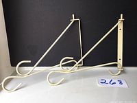 Pair of cream-colored metal gardening plant hangers designed for mounting on fence or wall, showing full items and design details