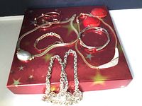 Photo of gold-tone costume jewelry including chain link bracelet, multiple bangle bracelets, pendant necklace with faux pearl, and pairs of earrings on a decorative red box