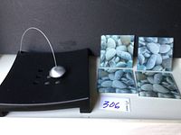Photo showing black IKEA napkin holder with wire and oval weight alongside four stone pattern glass coasters.