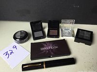 Photo of multiple single eyeshadow pots and a black and gold tube on a white surface