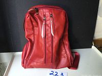 Front view of the red leather look backpack showing main and front zippered pockets.