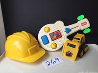 Photo showing yellow kids helmet, white Playskool Busy Guitar toy, and yellow toy bulldozer together