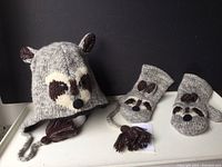 Full view of raccoon toque and mittens on a black background showing front raccoon face design, ear accents, and matching mittens.