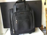Front view of black Samsonite travel bag showing dual handles, front pockets, and logo plaque.