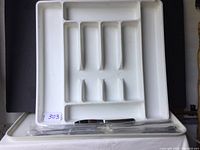 White plastic IKEA silverware tray with compartments for utensils and a dozen pieces of stainless steel silverware still in plastic wrapping inside the tray.