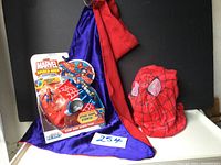 Spider Man Stunt Wing Spider Plane toy in packaging alongside red and purple cape and red Spider Man hood