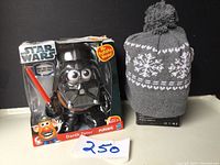Star Wars Darth Vader Mr. Potato Head toy in original packaging next to gray knitted toque with white snowflake pattern and pom-pom
