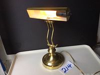 Front view of vintage brass table or piano lamp illuminated, showing adjustable neck and bulb housing.