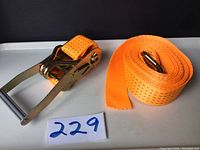 Photo of the new orange tie down ratchet strap showing strap rolled out and metal ratchet clasp mechanism.