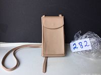 Front view of the beige travel bag with flap closure and thin strap laid on surface against a dark background.