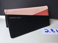 Closed travel document pouch showing color blocking with black, pink, and red sections and gold text 'TRAVEL DOCS'