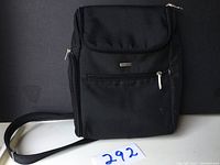 Front view of the black Travelon crossbody bag showing the bag's front zippered pocket, flap, and adjustable shoulder strap.