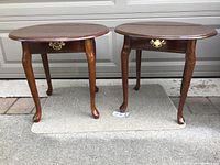 Two oval wooden French Provincial end tables side by side showing overall shape and style.
