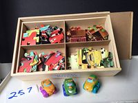 Wooden box with four compartments containing assorted wooden puzzle pieces and three small toy cars placed in front of the box.