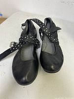 Pair of black Adrienne Vittadini ballet flats with cross strap and silver studs, size 9M, shown from a front angle on a white surface.