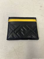 Front view of the black leather card holder with yellow accent and diagonal embossed pattern.
