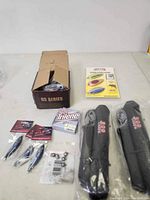 Full fishing lot with packaging box, jigging lures, fishing line, rod holders, metal spoons, and weights visible on a white surface