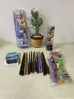 Full lot showing all items arranged on a white surface including doll, cactus toy, Hot Wheels car, Harry Potter wands, multi-colored ball tube, and small dinosaur toy.
