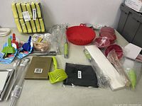 Overview of many kitchen accessories on table including scrub pads stack, silicone trays, ice cream molds, and cleaning tools.