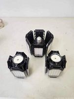 Three black LED garage light panels with foldable LED panels arranged in a triangular stance on a white surface.