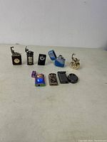 Photo showing nine refillable butane lighters in various shapes and finishes arranged on a plain surface.