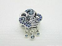 Front view of Pandora charm showing detailed cloud with embedded blue stones and a swallow figure in front of the cloud. Three blue teardrop-shaped stones hang below the cloud.