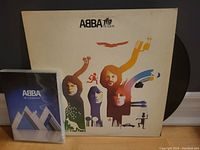 Vinyl record 'ABBA: The Album' partially visible with illustrated cover and ABBA 'In Concert' DVD case behind it.