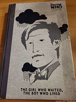Front cover of the hardcover graphic novel showing stylized artwork of a man's face with clouds, title 'The Girl Who Waited, The Boy Who Lived', and Doctor Who branding.