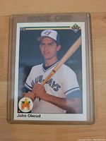 Front view of John Olerud rookie baseball card in top loader featuring him holding bat in Blue Jays uniform.