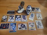 Full lot of Toronto Maple Leafs memorabilia including bobblehead, helmet, cards, and miniature goalie gear display on wooden floor