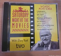 Front cover of the Saturday Night At The Movies CD with yellow/red graphics, featuring Elwy Yost and TVO branding, listing 14 classic movie love songs.
