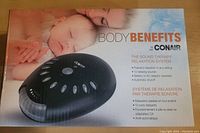 Top view of the original box showing the product name, brand, and key features in English and French, along with an image of the black sound therapy device with several oval buttons.