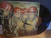 Front cover of The Who 'Odds & Sods' vinyl record showing band members in football helmets with 'ROCK' letters, with the record leaning beside it.