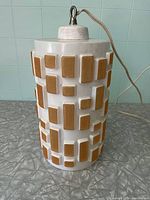 Full view of the white ceramic lamp showing orange rectangular geometric pattern and electrical cord attached at top.