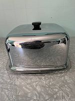 Side angle view of the chrome cover and part of the glass base showing the black handle on top and reflective surface under lighting.