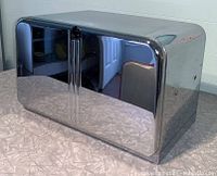 Front and side view of the chrome breadbox with reflective polished surface and vertical handle.
