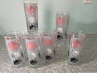 Front view showing six tall cylindrical highball glasses with pink, white, and black leaf designs on a frosted glass background.