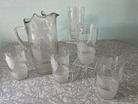 Full view of the glass pitcher surrounded by five matching glasses, all decorated with frosted floral motifs.