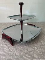 Side angled view of the two-tiered serving stand showing the polished metal trays and the Bakelite handles and support.