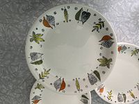 Top view of plates showing white base with colored leaf and floral pattern around the rim, stacked and spread slightly to show pattern detail and condition.